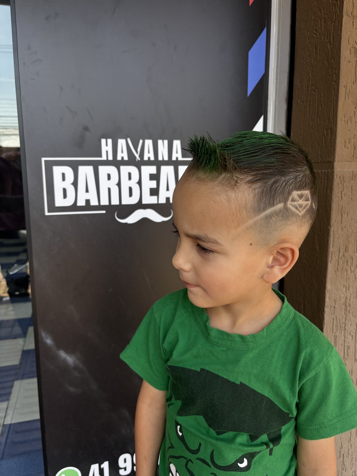 Criança com corte finalizado em frente ao banner da Havana Barbearia